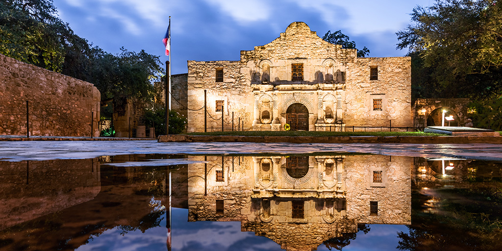 Evening image of the Alamo in San Antonio, with reflection pool in front casting a mirrored image of the structure