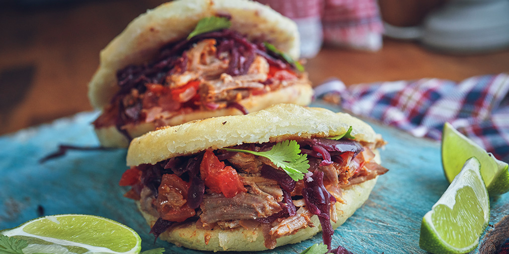 Arepas full of meat and vegetables on a bright blue plate